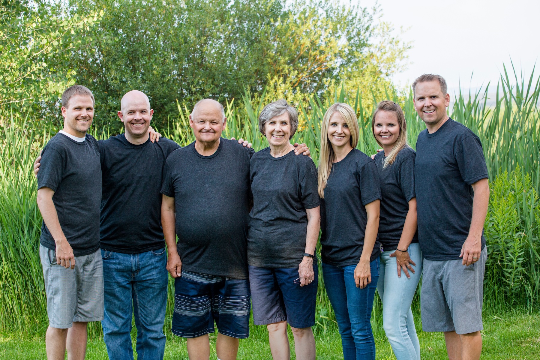 A senior couple stand smiling for a photo outdoors, alongside their five adult children.